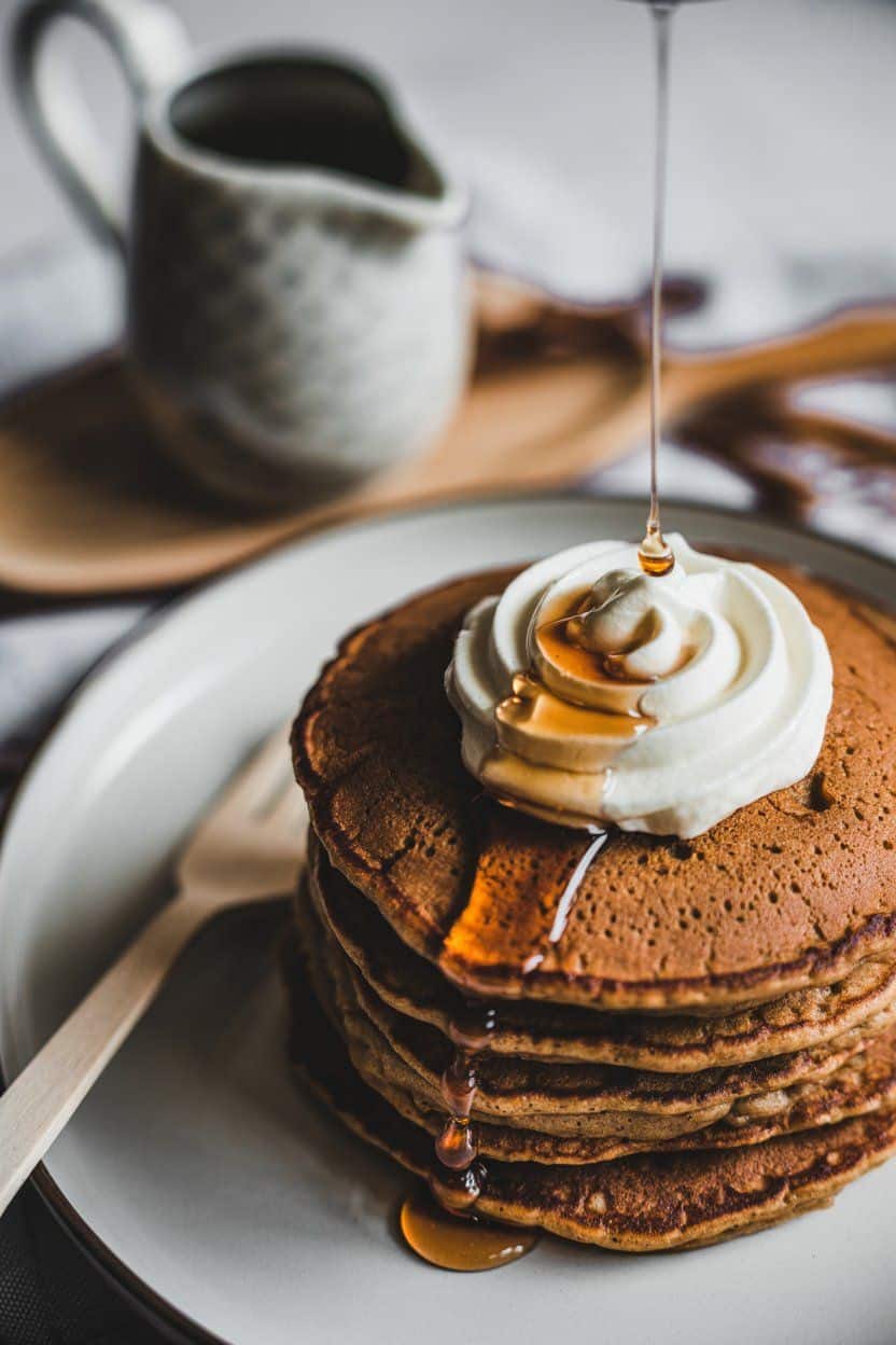 Stack of fluffy pancakes topped with whipped cream and syrup, perfect for a Christmas brunch.