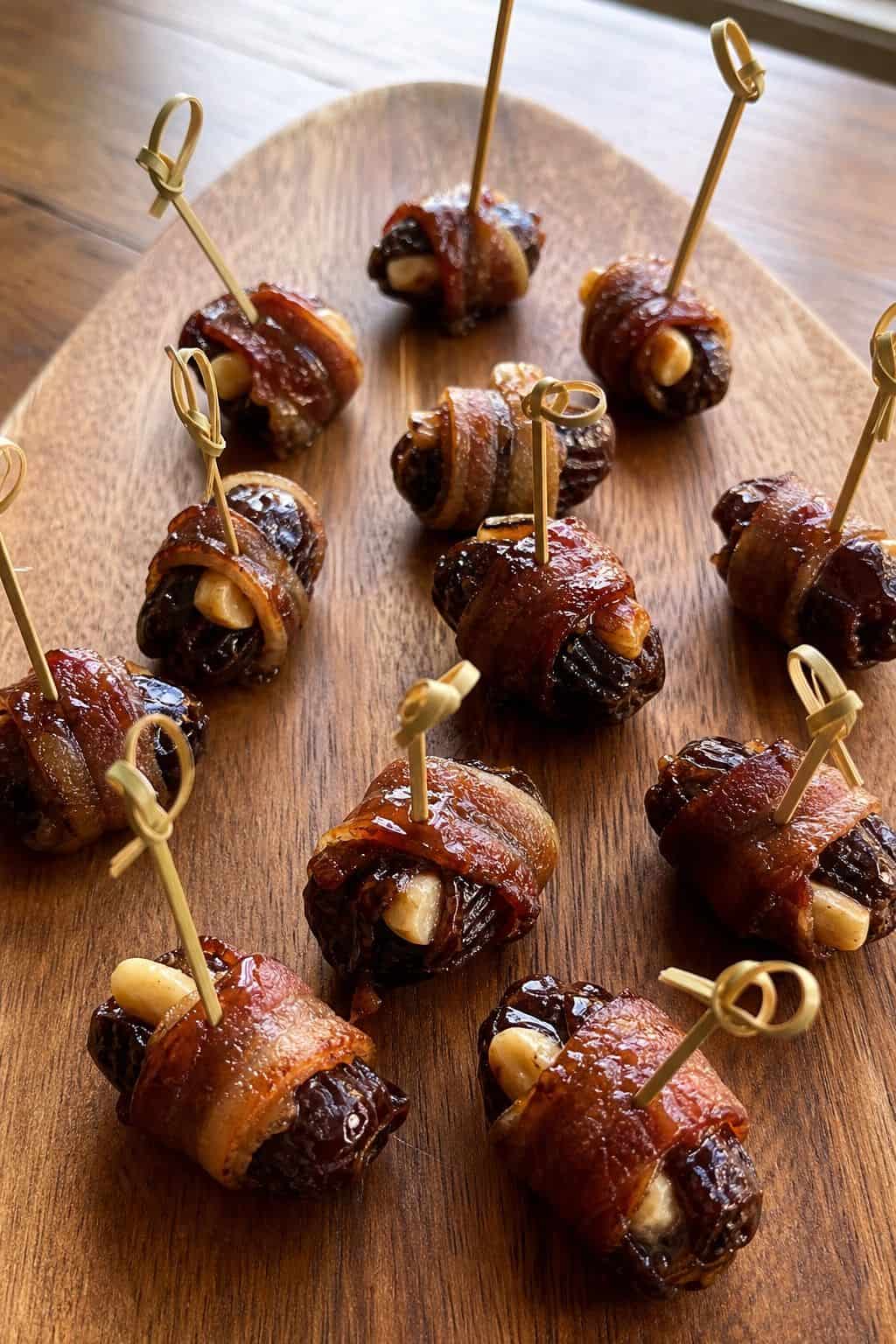 Bacon-Wrapped Dates Recipe Bacon-wrapped dates stuffed with manchego and marcona almonds on a wood serving board.