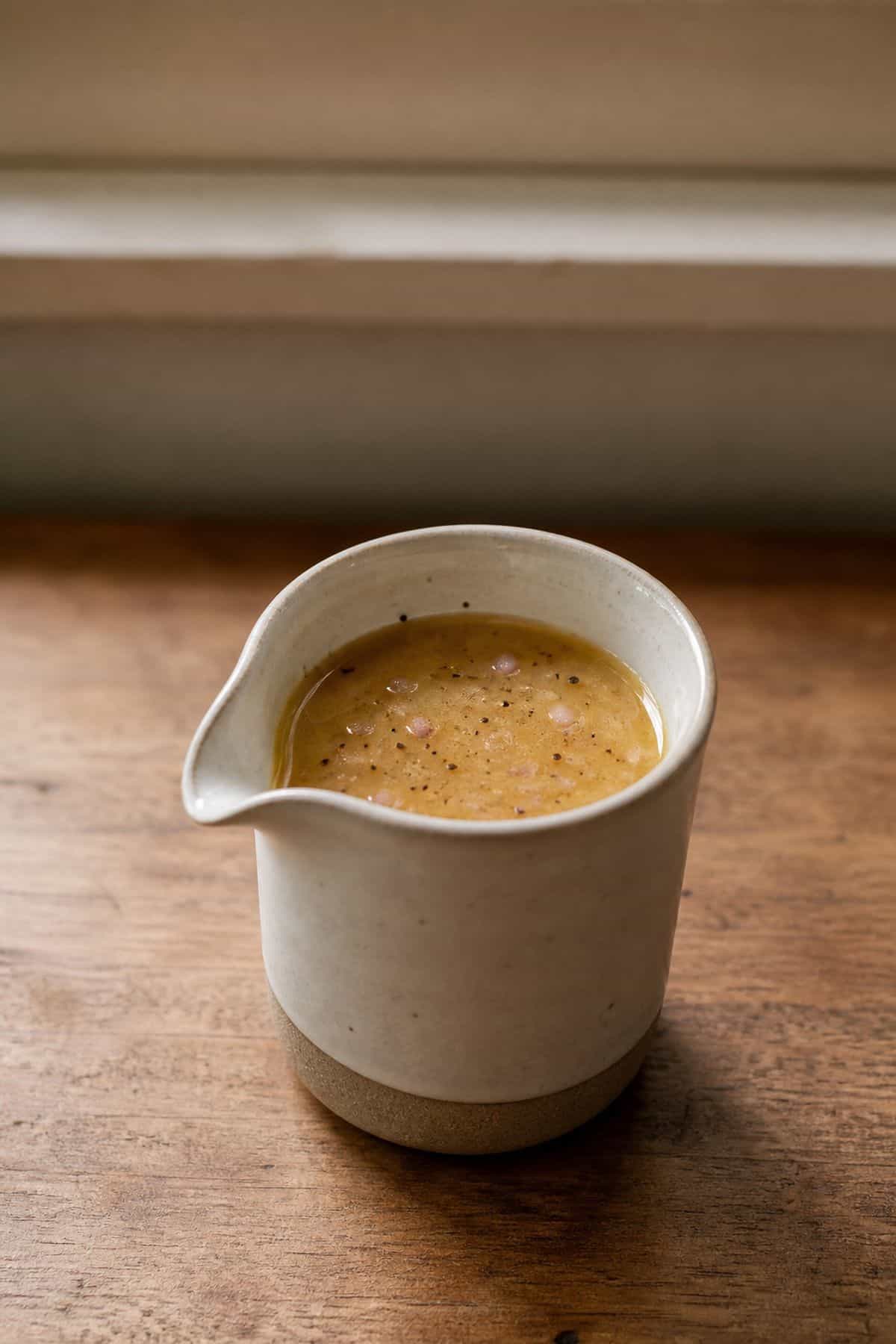 Classic sherry vinaigrette in a small ceramic pitcher with shallot and black pepper