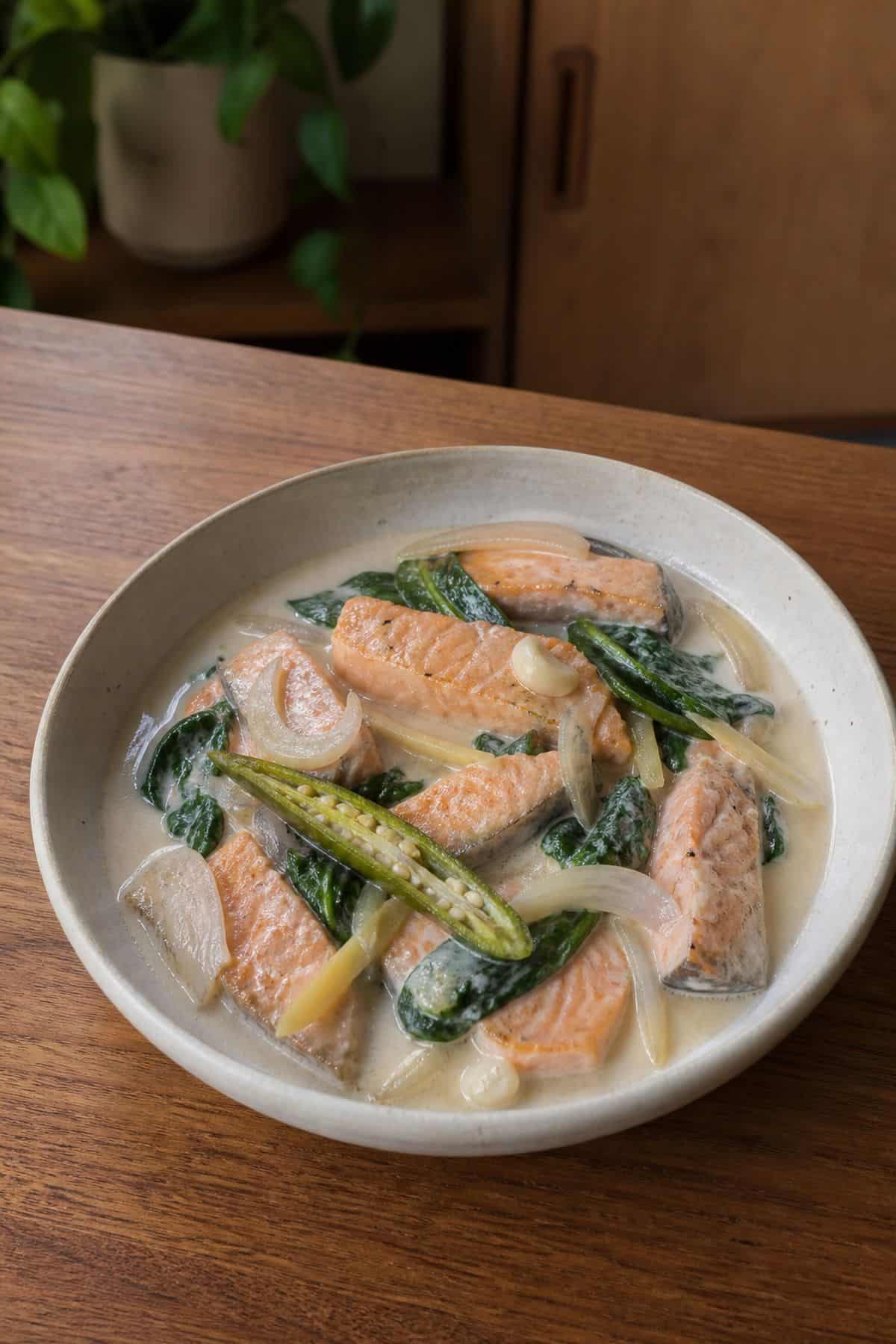 Filipino coconut salmon with creamy coconut sauce, wilted spinach, ginger, garlic, onion, and long green chili.