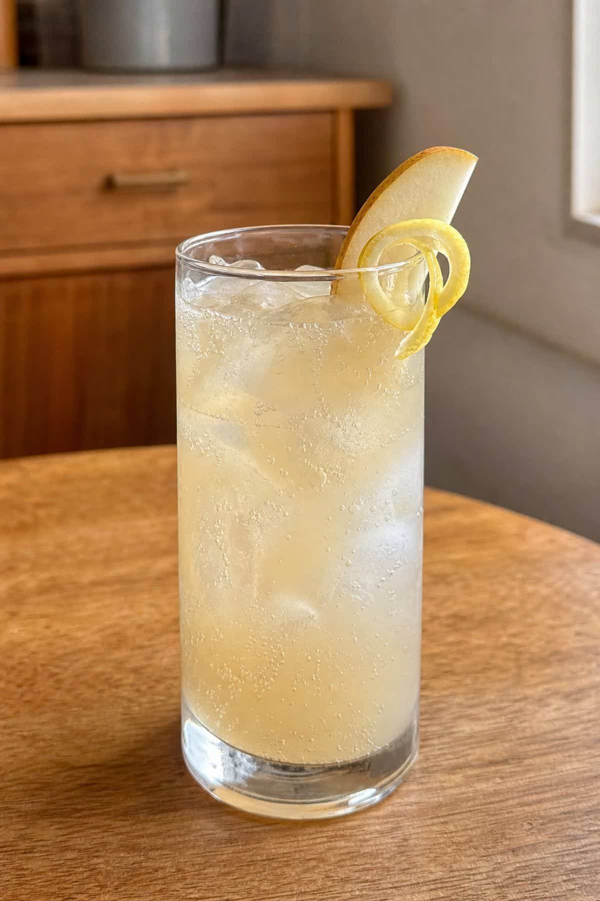 Ginger Pear Collins Cocktail Recipe for Every Season Ginger Pear Collins cocktail in a tall glass with pear slice and lemon twist