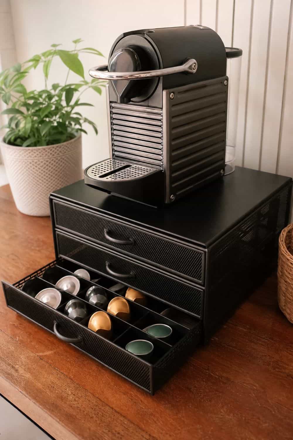 A low drawer organizer under the brewer visibly stores divided coffee capsules without loose boxes.