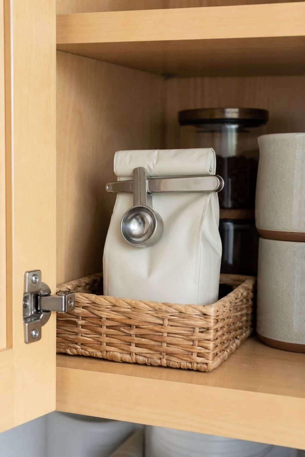 A tablespoon scoop clip closes a folded backup coffee bag and remains attached inside a clean cabinet basket.